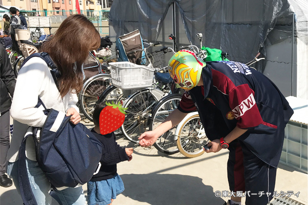 このイベント用に用意した新シールを子供たちに配布するマスクド東大阪